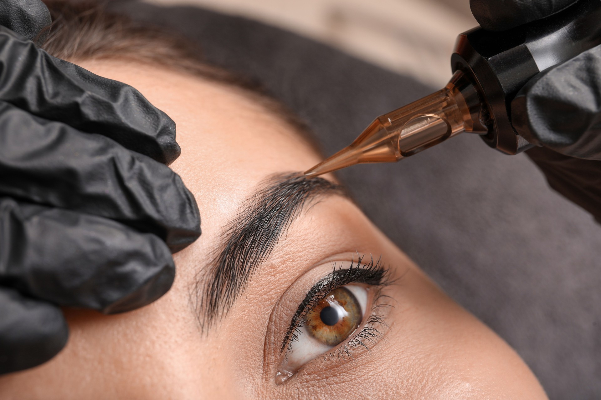 Young woman undergoing procedure of permanent eyebrow makeup in tattoo salon, closeup